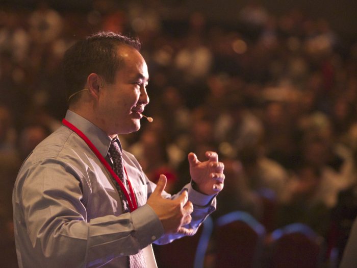 Dennis Yu speaking to an audience with a headset microphone
